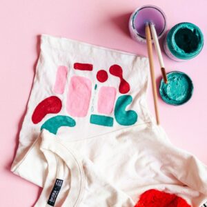 white and red crew-neck shirt beside paint with brushes